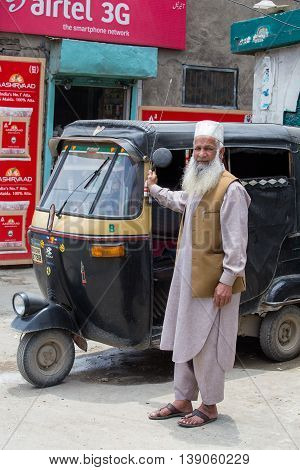 SRINAGAR INDIA - JULE 11 2015: Auto rickshaw taxis and muslim man on a road in Kashmir India. These iconic taxis have recently been fitted with CNG powered engines in an effort to reduce pollution