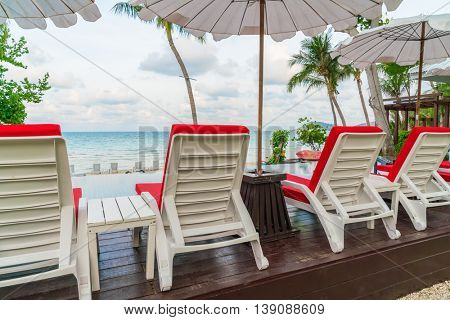 Beautiful beach chairs with umbrella around outdoor swimming pool neary sand and sea
