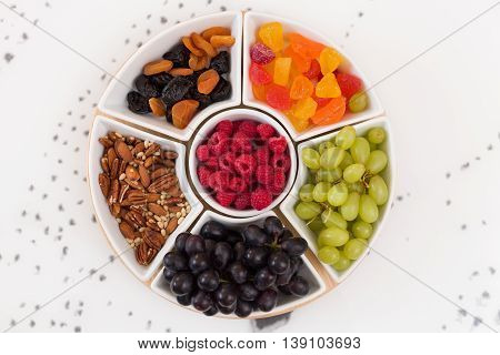 Round set of plates full of nuts raspberries sweets grapes and dry fruit on the white background. Healthy snacks. Desserts for coffee or tea. Assorted mix of pecans berries and fruit.
