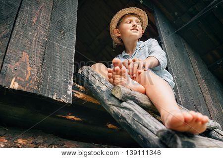 Barefoot boy sits on ladder in barn attic