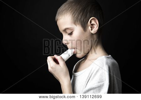 A Close up image of a cute little boy using inhaler for asthma.