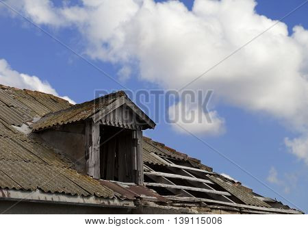 Old tile roof with holes and blue sky with clouds in sun day