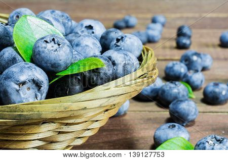 Freshly picked blueberries in wicker bowl. Juicy and fresh blueberries with green leaves on rustic table
