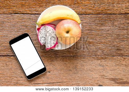 Smart phone with fruit (bananaappkedragon fruit) on wooden floor. Top view focus.