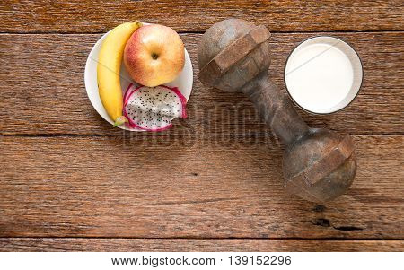 Iron dumbbell and milk with fruit (bananaappkedragon fruit) on wooden floor.Top view focus.