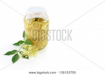 Sambucus nigra elderberry sirup with flower and leaves on white background. Pieces of elderberry with pieces of lemon in a glass of water.