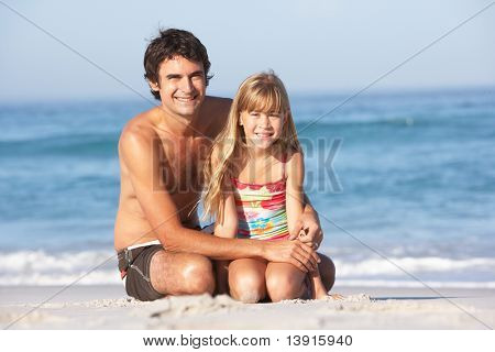 Père et fille portant des maillots de bain assis sur la plage de sable