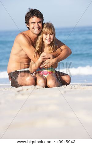 Père et fille portant des maillots de bain assis sur la plage de sable