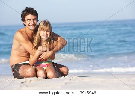 Père et fille portant des maillots de bain assis sur la plage de sable