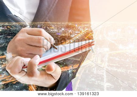 Double exposure of businesswoman  writing the word on a notebook on night cityscape background.