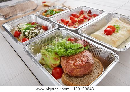 Healthy restaurant food delivery in foil box. Green stewed cabbage roll with veal steak on brown bread and other dishes. Beef and vegetable with cherry tomato. Meals take away closeup.