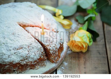 Birthday party. Birthday in yellow style. Home cake. Piece of cake with a lighted candle on a wooden table yellow rose and ribbon