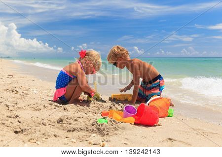 little boy and girl play with sand on summer beach