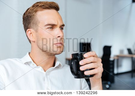Serious concentrated young businessman drinking coffee in offiice