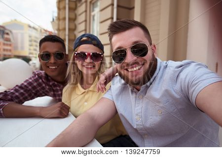 Picture of happy friends posing for camera. Happy peole making selfies on mobile or smart phone outdoors. People spending free time in city centre.