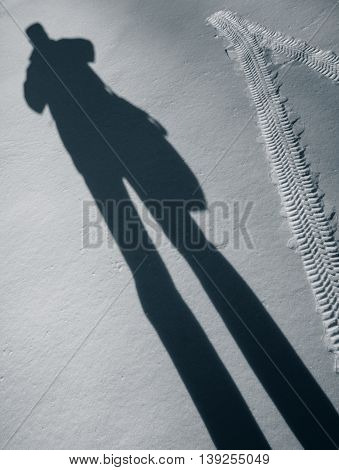 Automobile tire footprint and shadow of a man in the snow