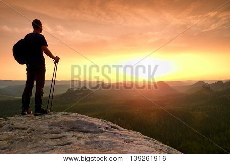 Man With Tourist Poles In Hand And Sporty Backpack Above Valley.