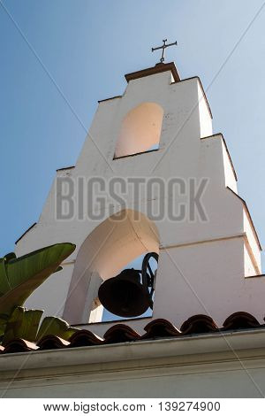 Bell in motion at Mary, Star of the Sea Catholic Church, La Jolla, California. Steeple has cross. The Contemporary Spanish Mission design was selected for this building, constructed in 1906 on Girard Street.