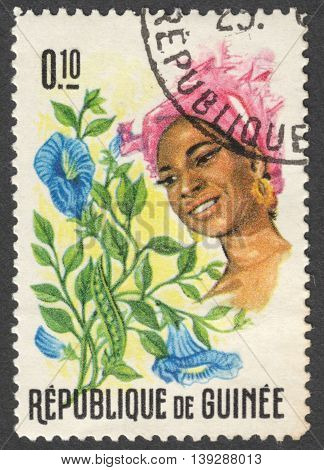 MOSCOW RUSSIA - CIRCA JANUARY 2016: a stamp printed in GUINEA shows a woman in the traditional headdress and a plant Clitoria sp. the series "Guinean Flora and Female Headdresses" circa 1966