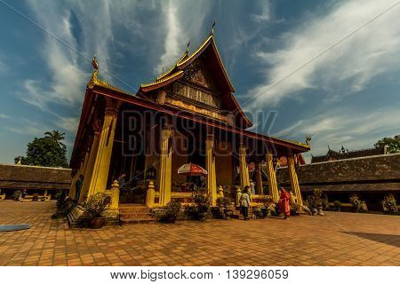 A monk talks to two people at the golden Wat Si Saket in Vientiane, Laos