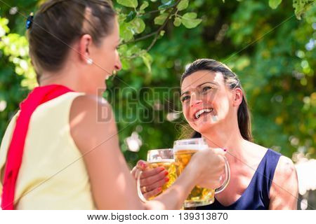 Women in beergarden having refreshment sitting under tree in the shade as it is hot