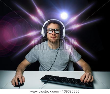 technology, gaming, entertainment, let's play and people concept - young man in headset and eyeglasses with pc computer playing game and streaming playthrough or walkthrough video over light