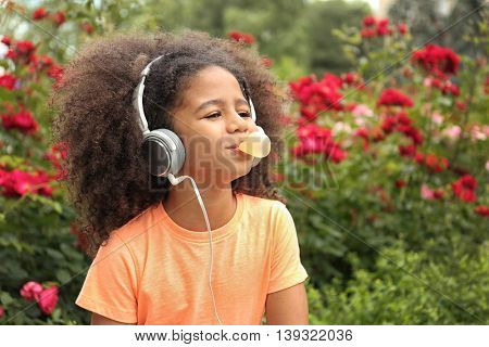 Afro-American little girl with sunglasses and headphones chewing bubblegum in park