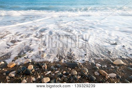 Sea waves crashing on the shore and flowing above seashore pebbles.