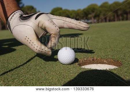 close up of man's hand putting golf ball in hole at course
