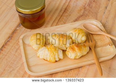 small tasty croissants on wooden dish near spoon and fork with honey in a jar.