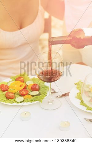 Toned picture of sommelier pouring red wine in the glass. Professional sommelier pouring red wine for beautiful woman in restaurant or cafe.