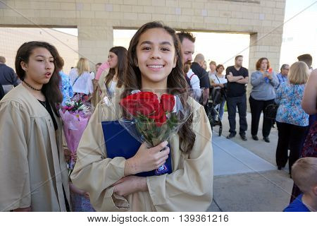 JOLIET, ILLINOIS / UNITED STATES - MAY 19, 2015: A girl proudly holds her diploma, and a bouquet of red roses, after an eighth grade graduation ceremony held at Plainfield South High School.