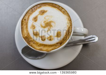 A cup of cappuccino with a decorative pattern, spoon on the saucer