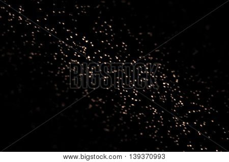 Abstract black glitter texture on a black background. Gold shiny dots over dark backdrop. Defocused Christmas lights