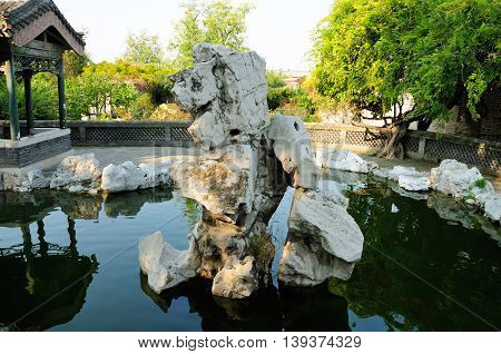 A large rock with a small pond within the traditional chinese garden on the Kong Family mansion property in the city of Qufu lcoated in Shandong Province China.