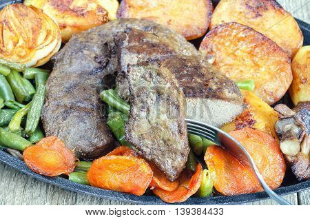 Fried beef liver with vegetables, close-up. Halves of potatoes, onions, whole mushrooms, carrots and green beans