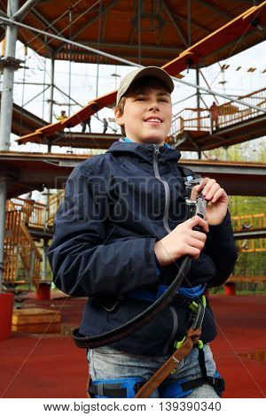 Smiling boy holds safety rope near Rope way on special playground