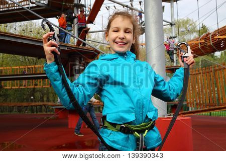 Smiling pretty girl holds safety rope near Rope way on special playground