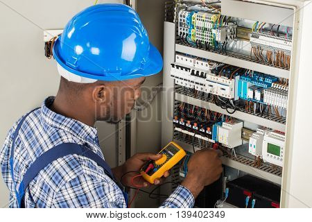 Young African Male Technician Examining Fusebox With Multimeter Probe