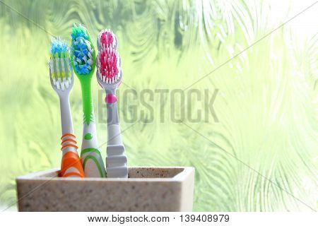 Three Toothbrushes In A Clay Tumbler In The Morning Light Of An Obscured Window