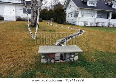 Artesian spring water flows through a narrow channel between houses in Wequetonsing, Michigan, and into a culvert below a decorative bench, towards Little Traverse Bay.