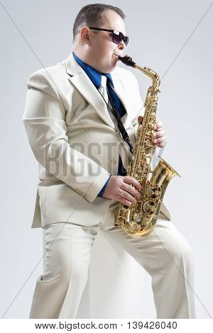 Portrait of Hadnsome Male Saxophone Player Playing in Studio Environment. Wearing Stylich Suit and Sunglasses. Vertical Image Orientation