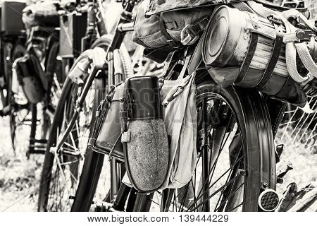 Old military bicycle with kitbag and equipments. Backpack and containers for food and drink. Vintage scene. Black and white photo. Retro transport. Equipment of german soldier in World War II.