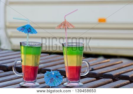 Two glasses with colorful cocktails and straws on a wooden lounger on the background Autocamper