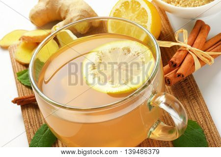 close up of cup of ginger tea with lemon, fresh ginger and cinnamon on wooden cutting board