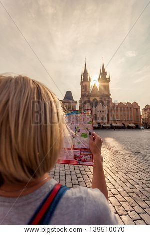 PRAGUE, CZECH REPUBLIC - JUNE 05, 2016: Woman looks at map in the old town square. Travel guide, tourism in Europe, female tourist with map. Kostel Panny Marie pred Tynem. Church of the Virgin Mary.