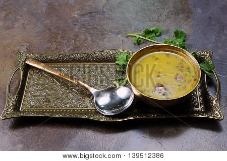 Yellow Lentil soup or Arhar Daal fry with the tadka of cumin seeds garlic and green chilies in a bowl on a tray with cilantro leaves on the side with copy space selective focus.