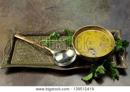 Yellow Lentil soup or Arhar Daal fry with the tadka of cumin seeds garlic and green chilies in a bowl on a tray with cilantro leaves on the side with copy space selective focus.
