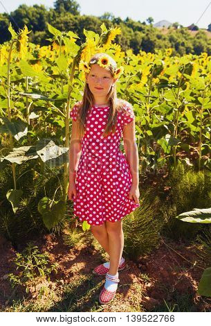 Little girl playing in sunflower fiield on a very hot summer day, wearing red polka dot dress and shoes, yellow flowers headband