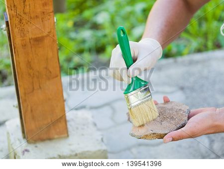 Man with protective glove sticking with putty knife broken stone to obtain refreshment of garden resting place.